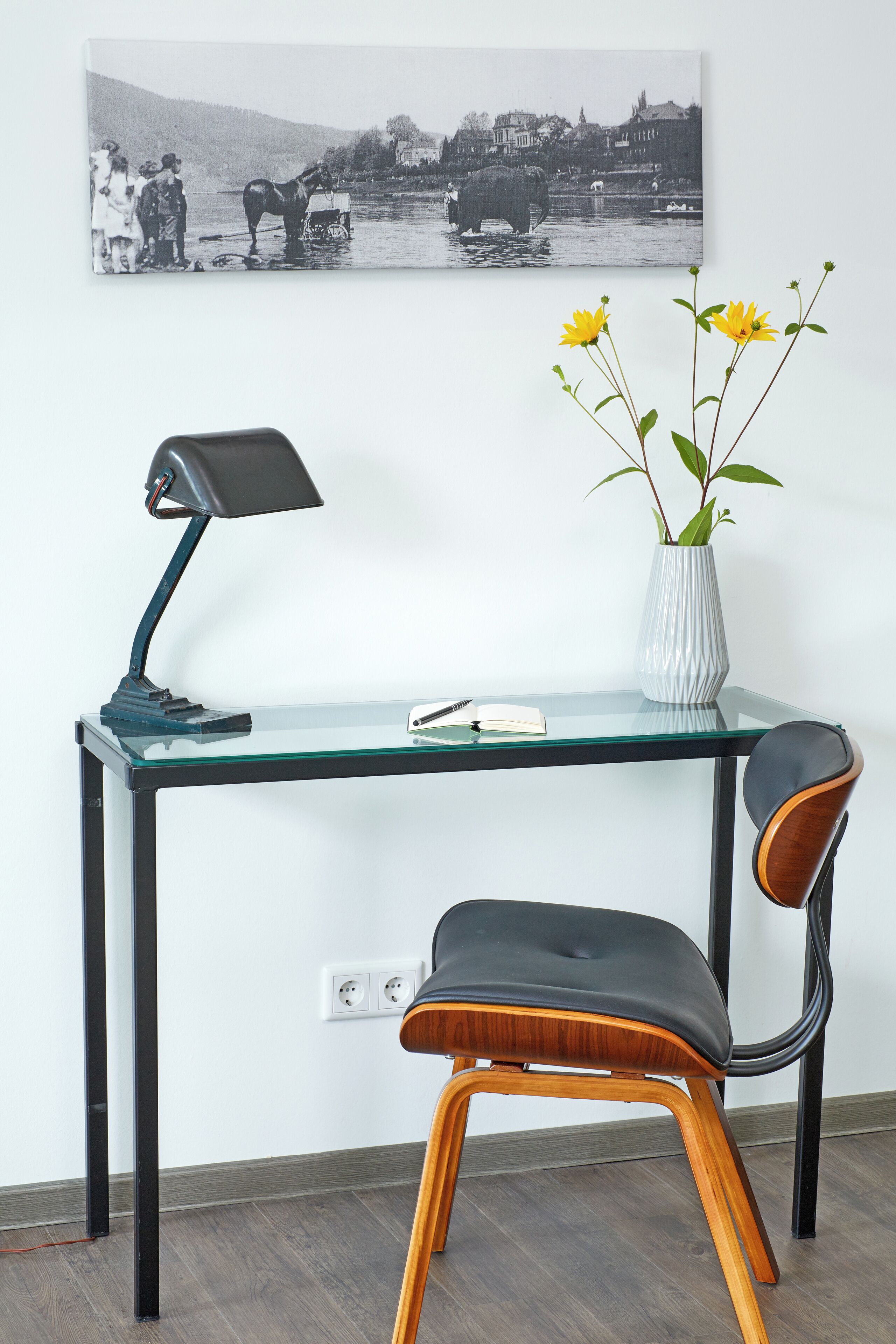 A modern desk with a lamp, a vase with flowers, and a chair.
