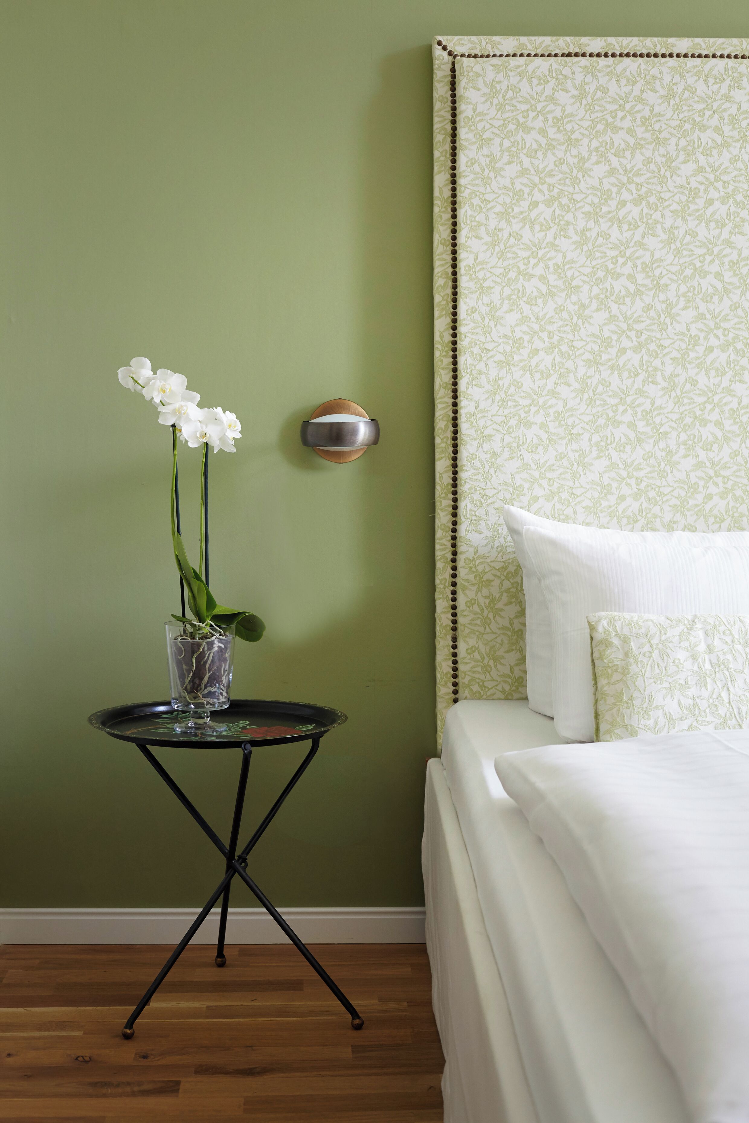 Ein Schlafzimmer mit einem Bett, einem Nachttisch und einer Vase mit weißen Blumen.