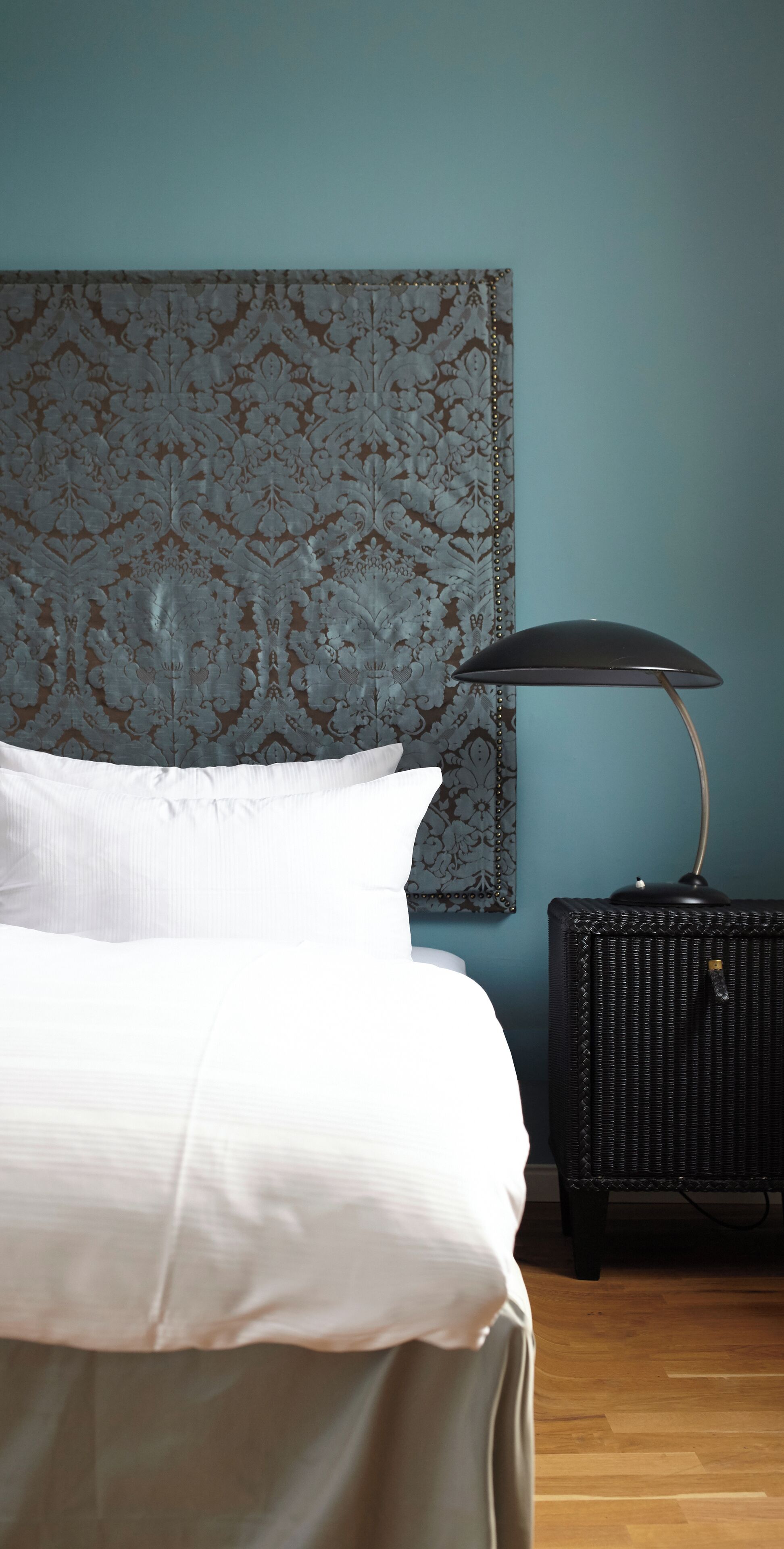 A bedroom with a bed, a headboard with a floral pattern, a lamp, and a nightstand.