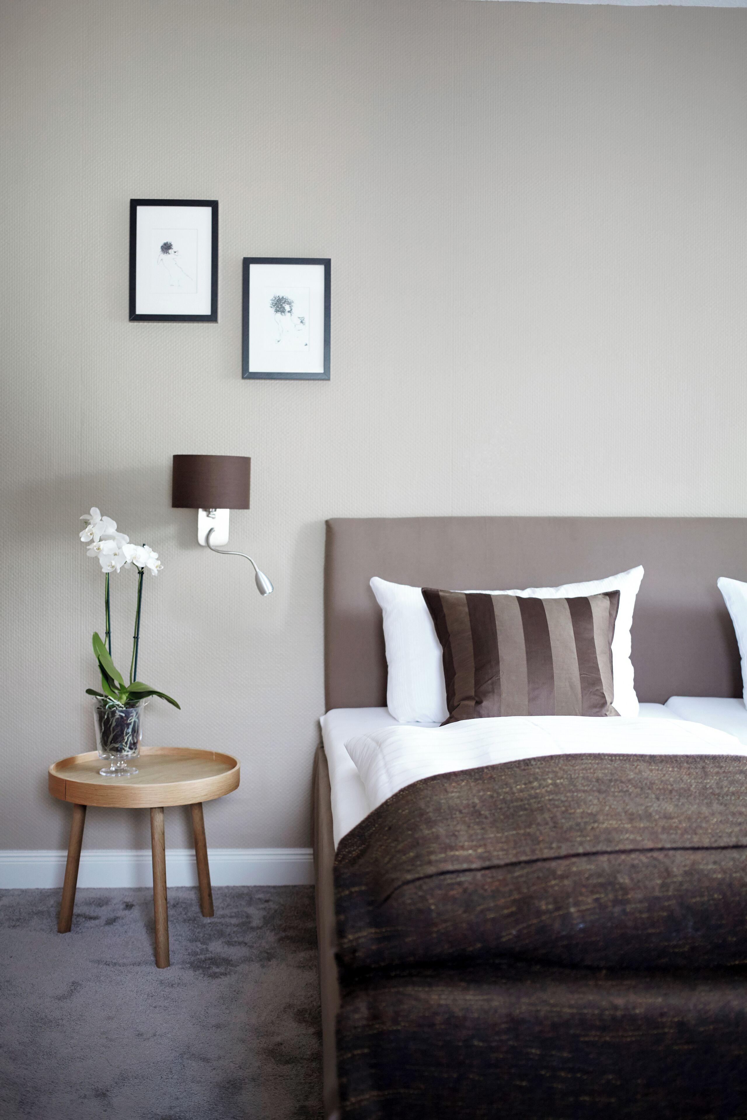 Un dormitorio con una cama, una mesita de noche con un florero y dos cuadros en la pared.
