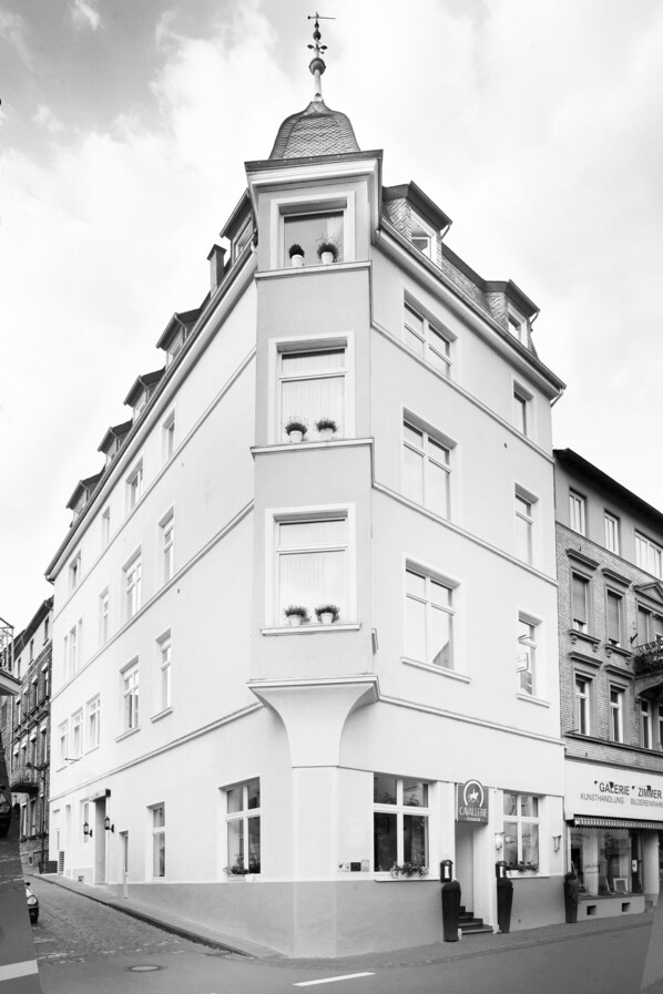 Un edificio en esquina con fachada blanca, varias ventanas y un pequeño balcón.