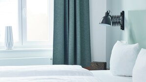 A neatly made bed with white linens, a dark grey headboard, and a wall-mounted lamp.