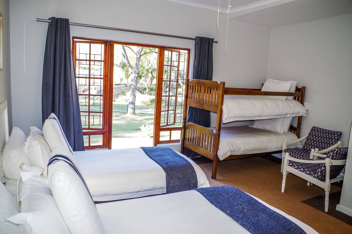 Une chambre d’hôtel avec un grand lit, un lit plus petit, une chaise en bois et une vue sur l’extérieur grâce à une porte coulissante.