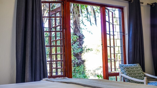 Une pièce avec un lit, une chaise et une fenêtre donnant sur un paysage verdoyant.