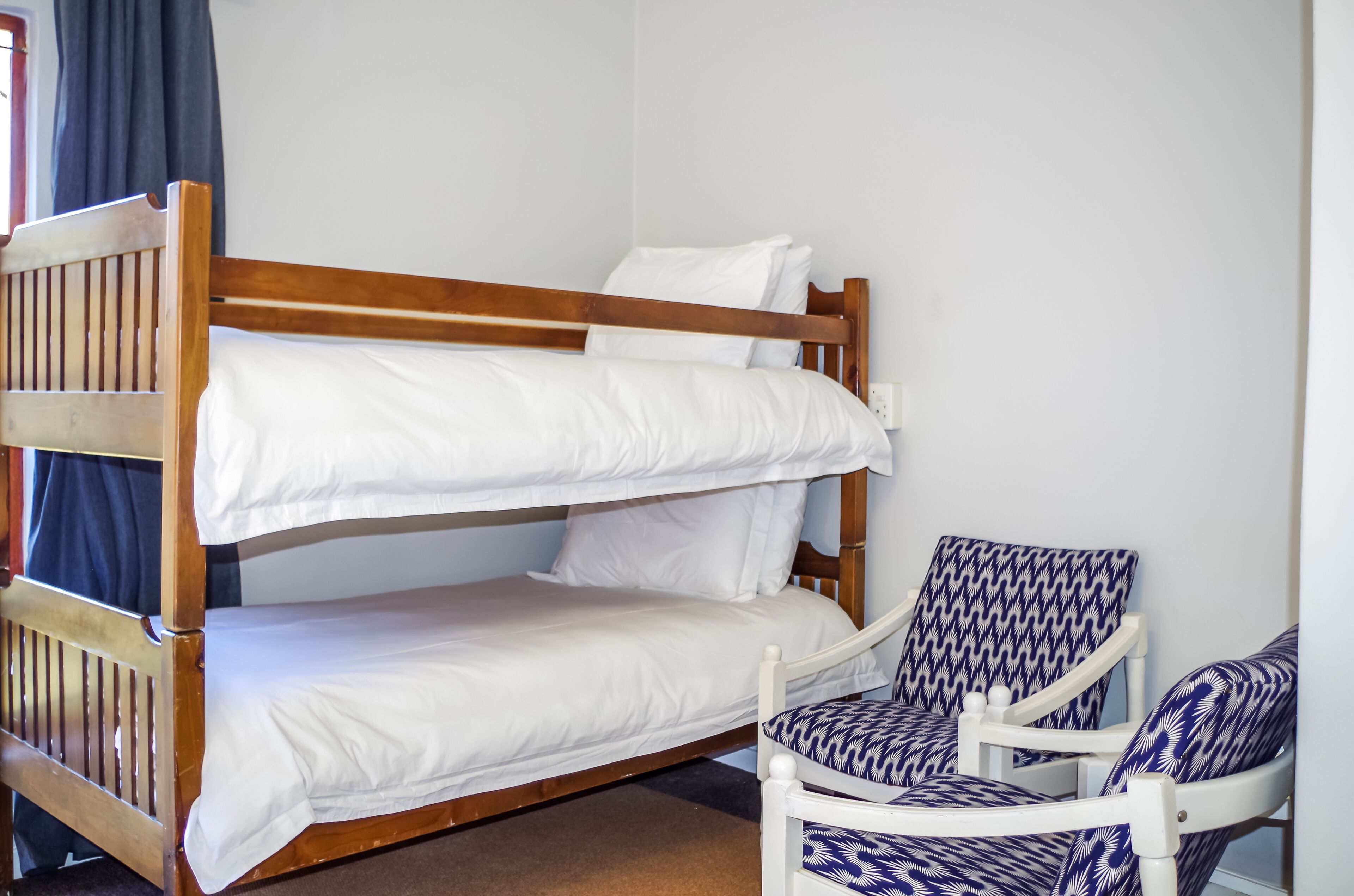 Una cama litera con ropa blanca y un sillón estampado.