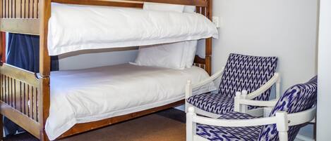 Una cama litera con ropa blanca y un sillón estampado.