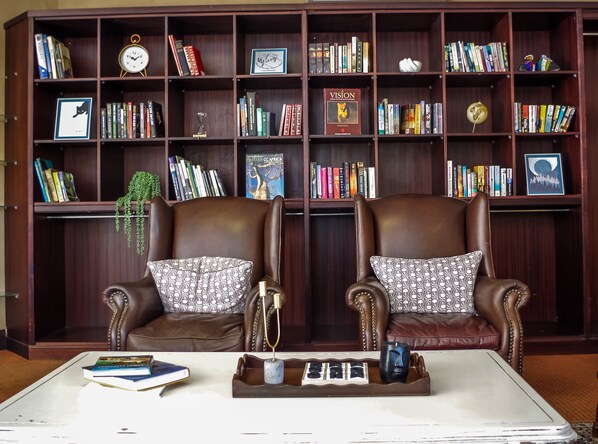 Una biblioteca con dos sillones de cuero, una mesa de centro y una estantería llena de libros y objetos decorativos.