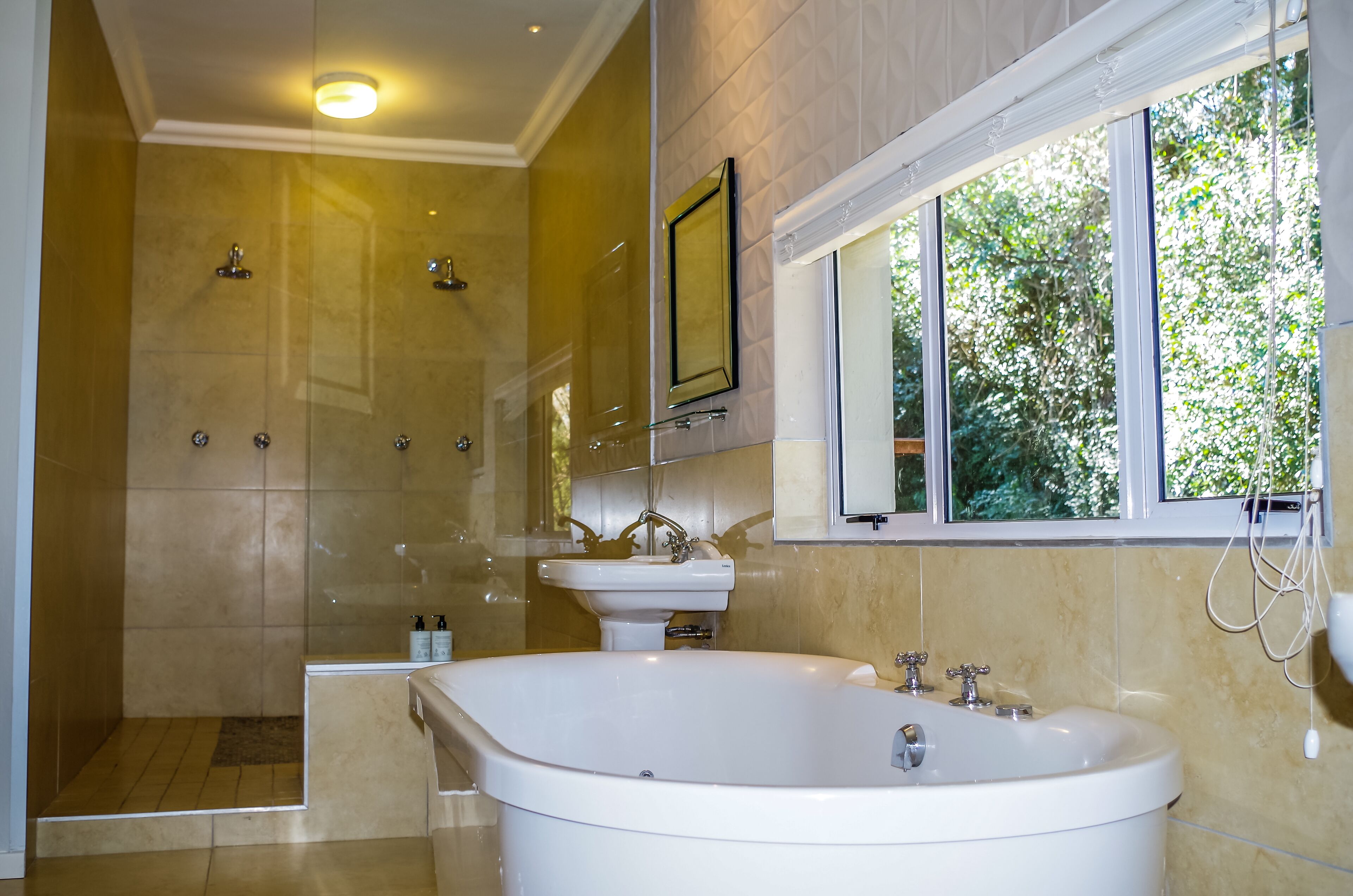 Een moderne badkamer met een inloopdouche, een vrijstaand bad en een groot raam dat voor natuurlijk licht zorgt.