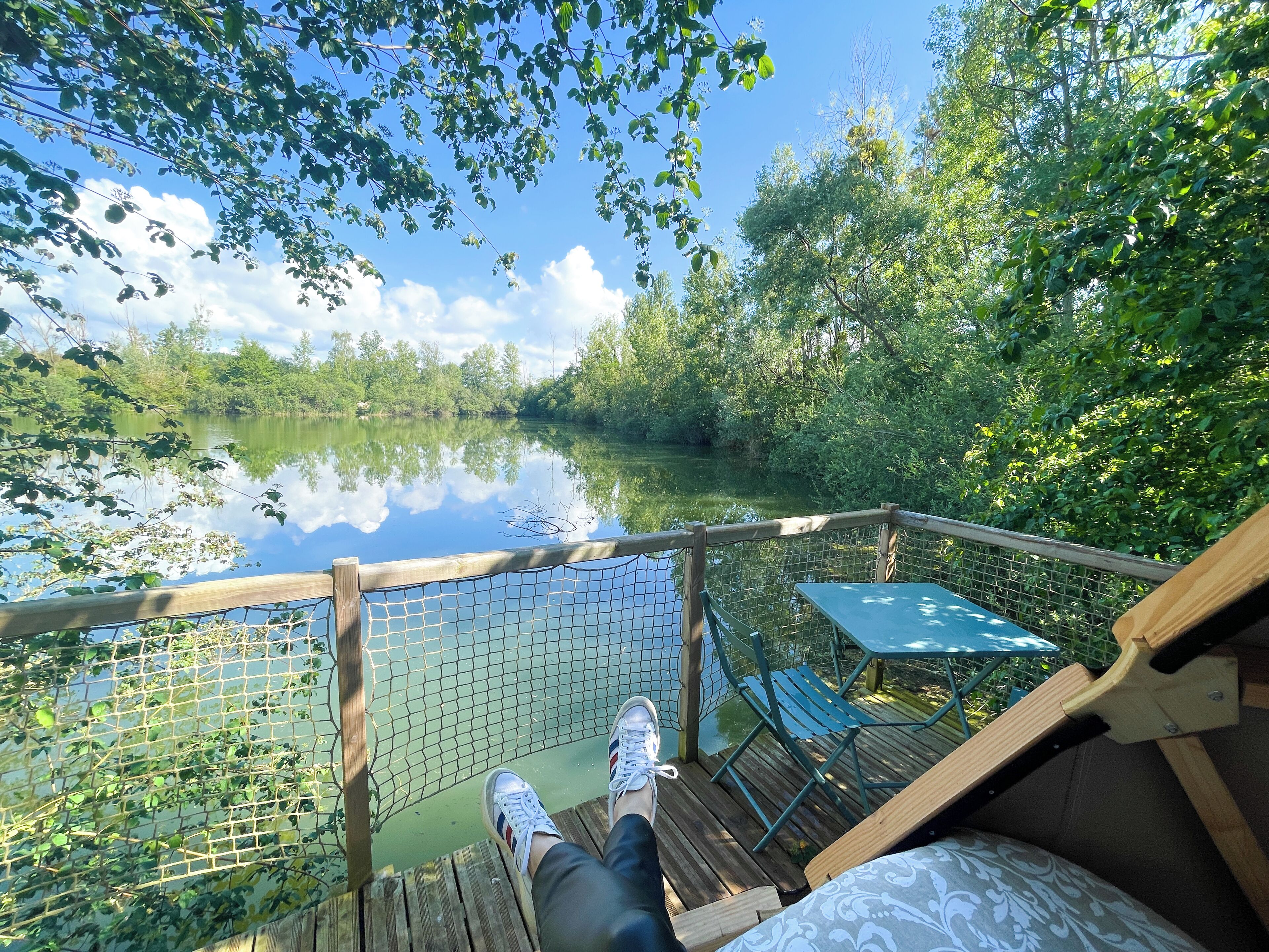 A wooden deck with a view of a calm lake, surrounded by lush greenery.
