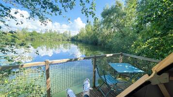 Una terraza de madera con vista a un lago tranquilo, rodeada de exuberante vegetación.