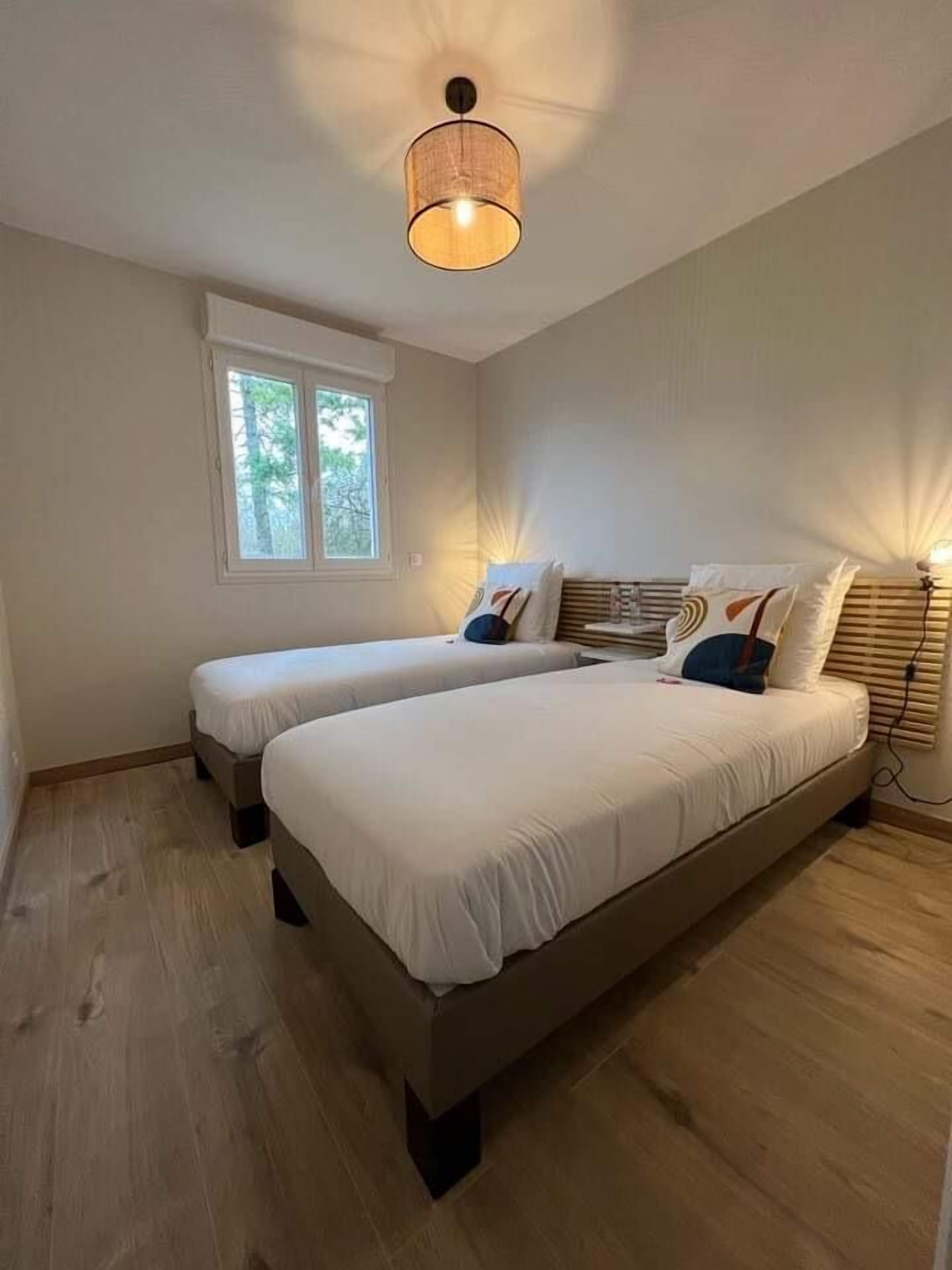 A bedroom with two beds, a window, and a ceiling light fixture.