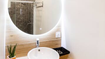 A modern bathroom with a round mirror, a white sink, and a wooden vanity.