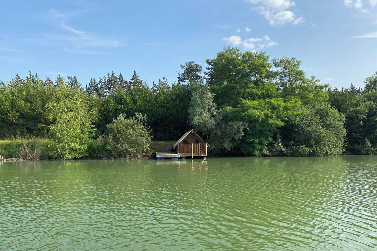 Una cabaña de madera sobre pilotes en un lago rodeado de árboles densos.