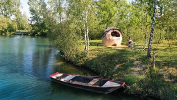 A river with a boat tied to the shore, a tent-like structure, and a person sitting on a chair.