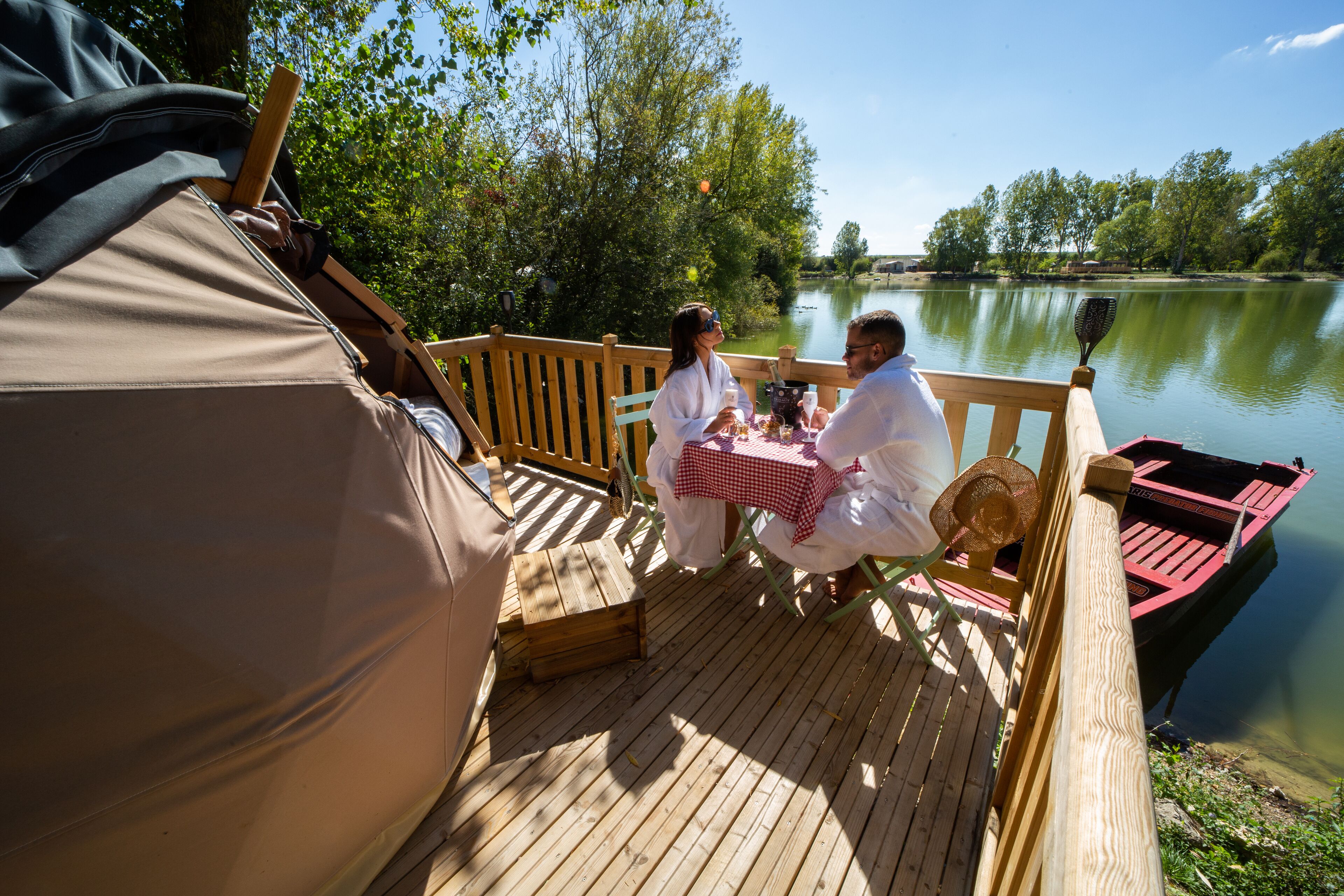 Una terraza de madera con una mesa y sillas, con vista a un lago tranquilo.