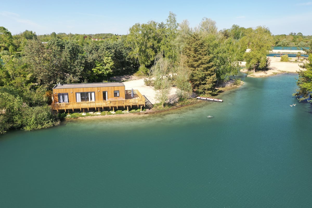 Una cabaña de madera junto a un río, rodeada de árboles.