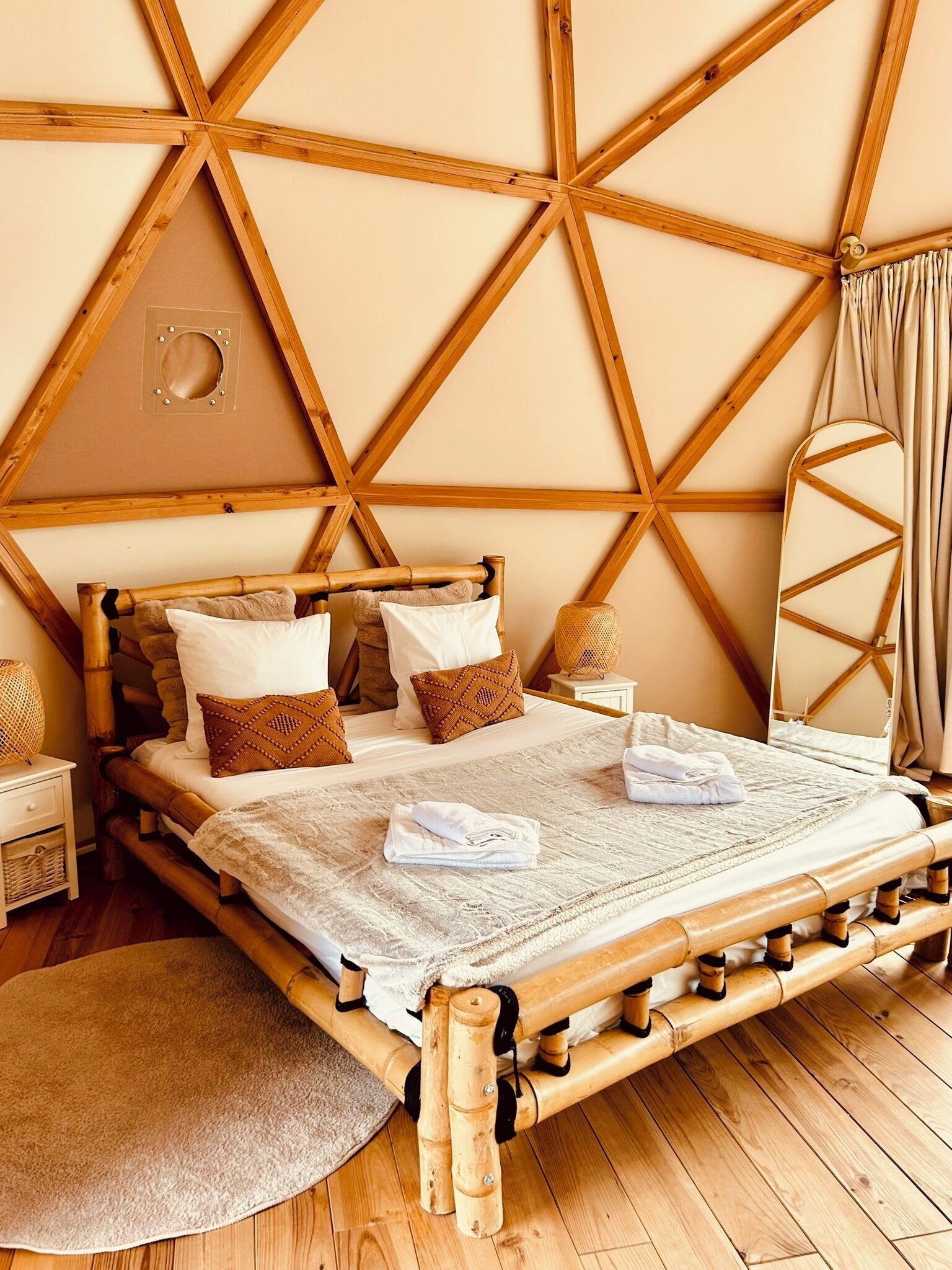 A room with a wooden bed, a round mirror, and a circular window.