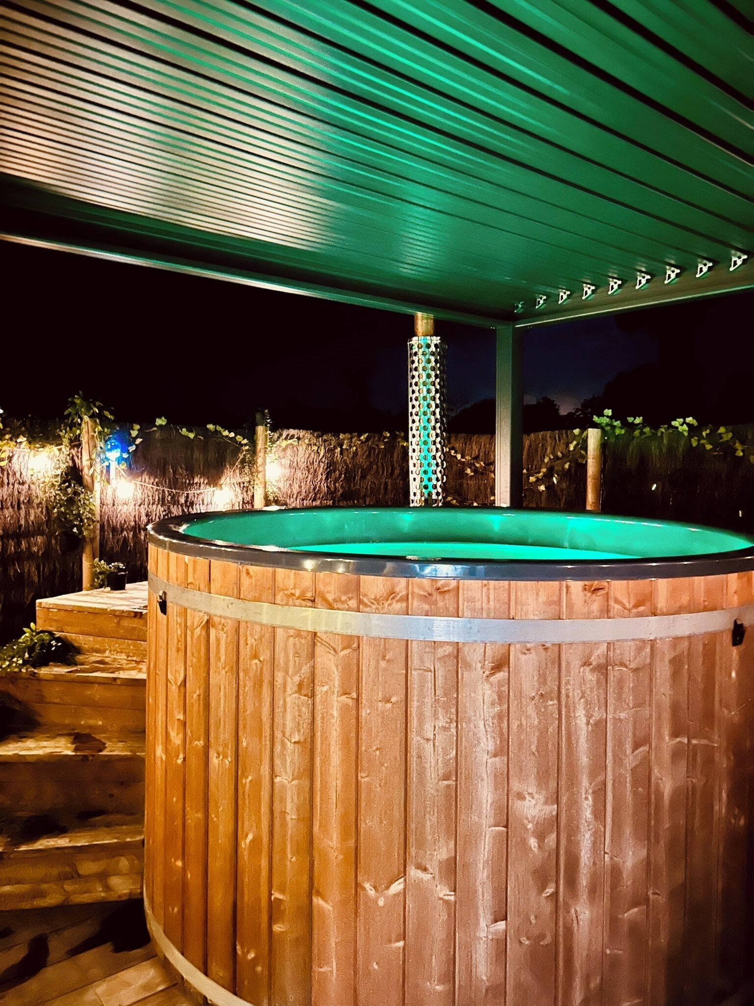 Un bain à remous en bois installé sous une terrasse couverte, agrémentée d’une colonne décorative.