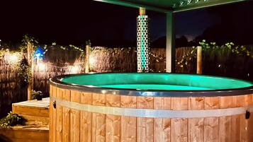 Un bain à remous en bois installé sous une terrasse couverte, agrémentée d’une colonne décorative.