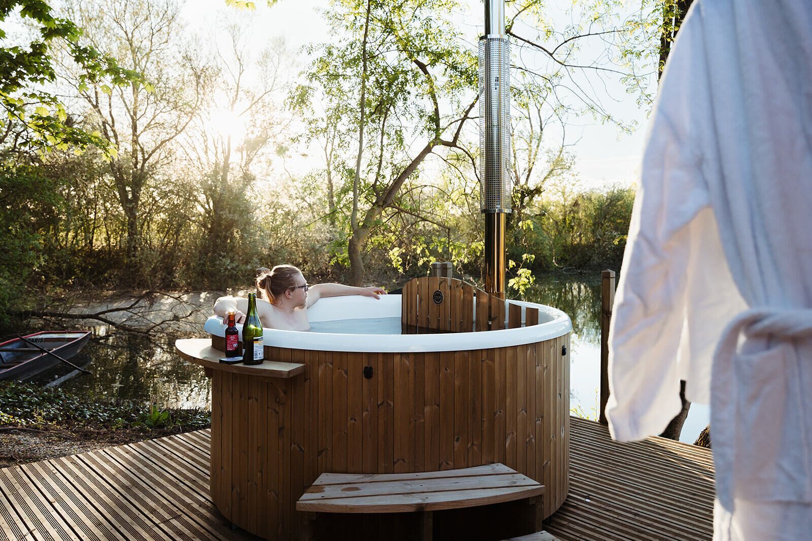 A hot tub with a wooden exterior, surrounded by a deck, and a body of water in the background.