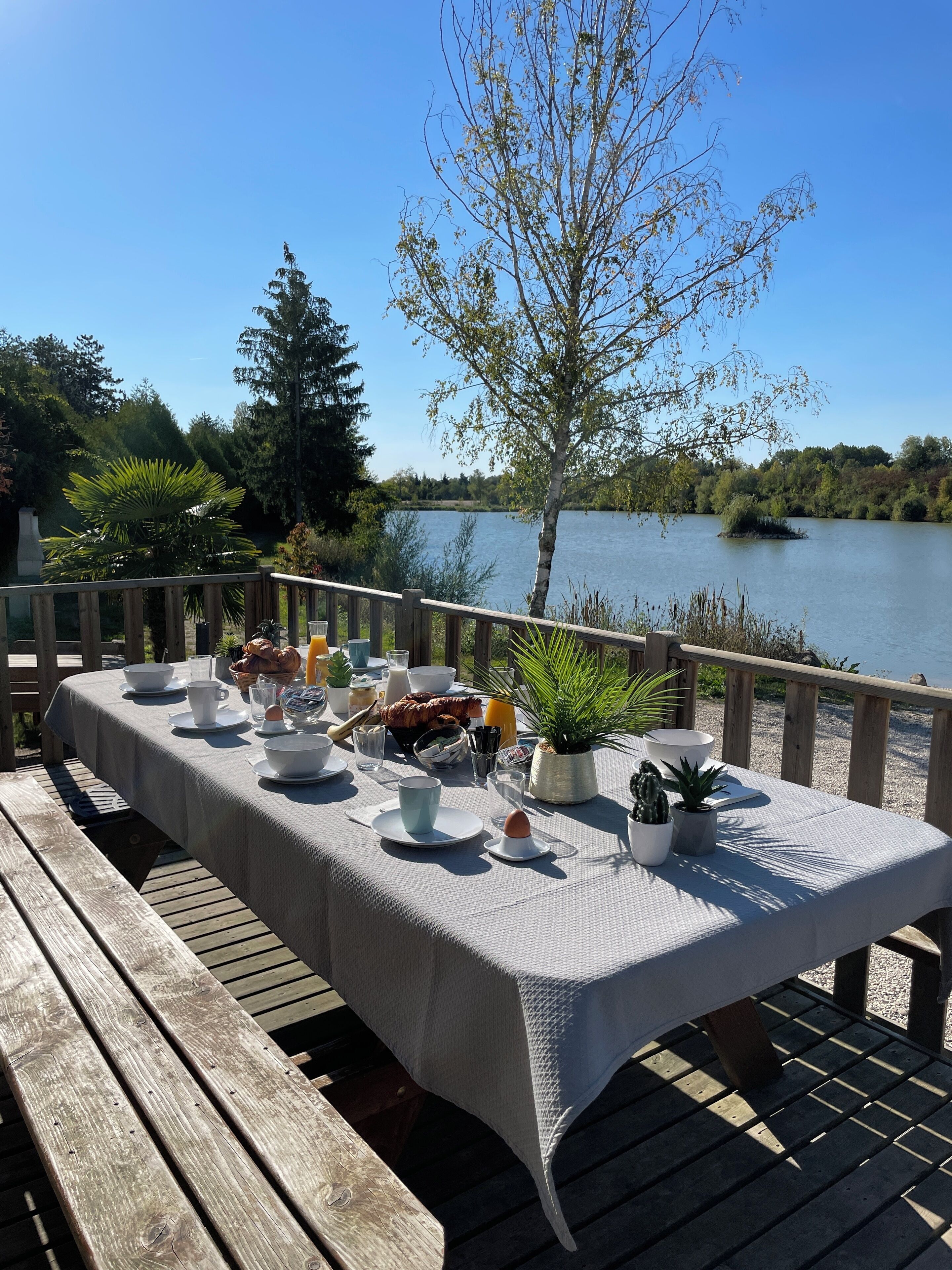 Eine Holzterrasse mit Frühstückstisch mit Blick auf einen See.