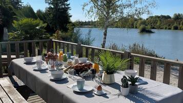 Eine Holzterrasse mit Frühstückstisch mit Blick auf einen See.