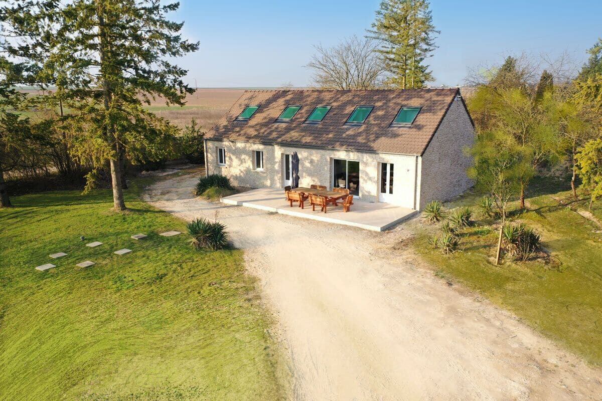 Una casa de una planta con entrada pavimentada y un patio con mesa y sillas.