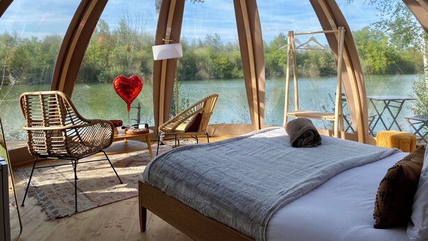 Una habitación acogedora y circular con una cama, dos sillones de mimbre, una mesa y un globo en forma de corazón colgando.