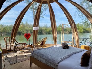 Una habitación acogedora y circular con una cama, dos sillones de mimbre, una mesa y un globo en forma de corazón colgando.