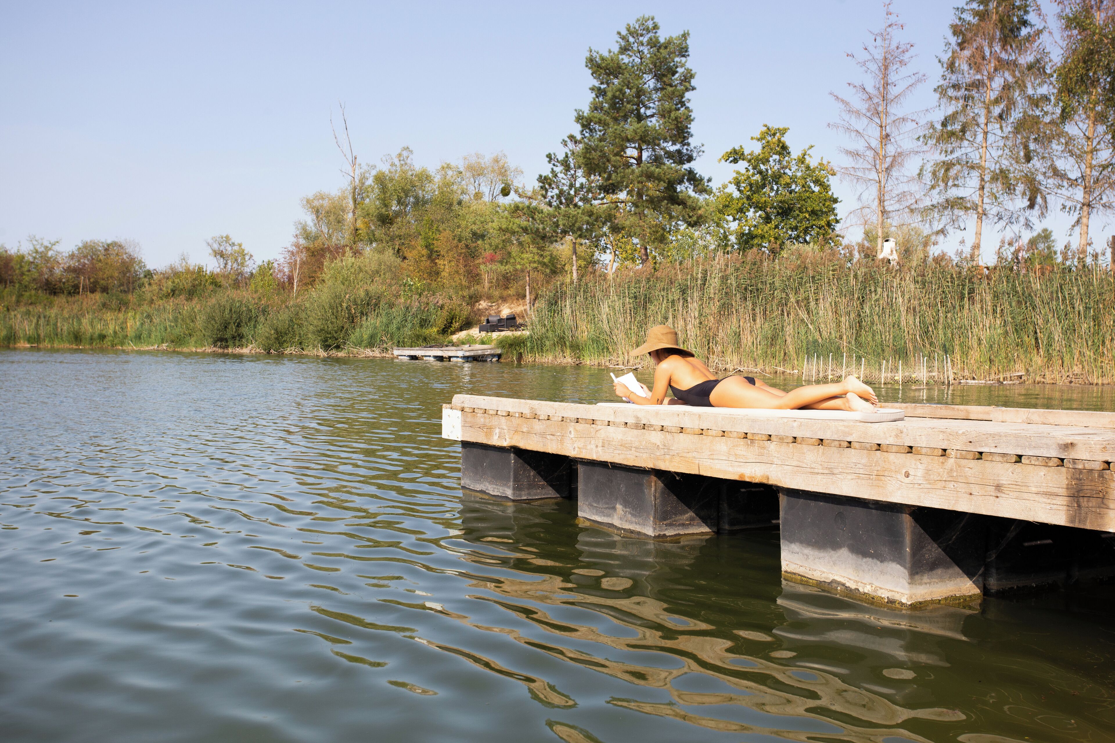 Een houten steiger die uitsteekt in een rustig wateroppervlak, met iemand die een boek leest.