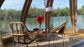 Una habitación acogedora con vista a un lago, que incluye sillones de mimbre, una mesita y un globo con forma de corazón.