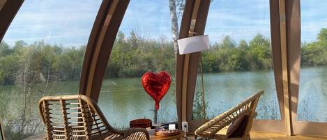 Una habitación acogedora con vista a un lago, que incluye sillones de mimbre, una mesita y un globo con forma de corazón.