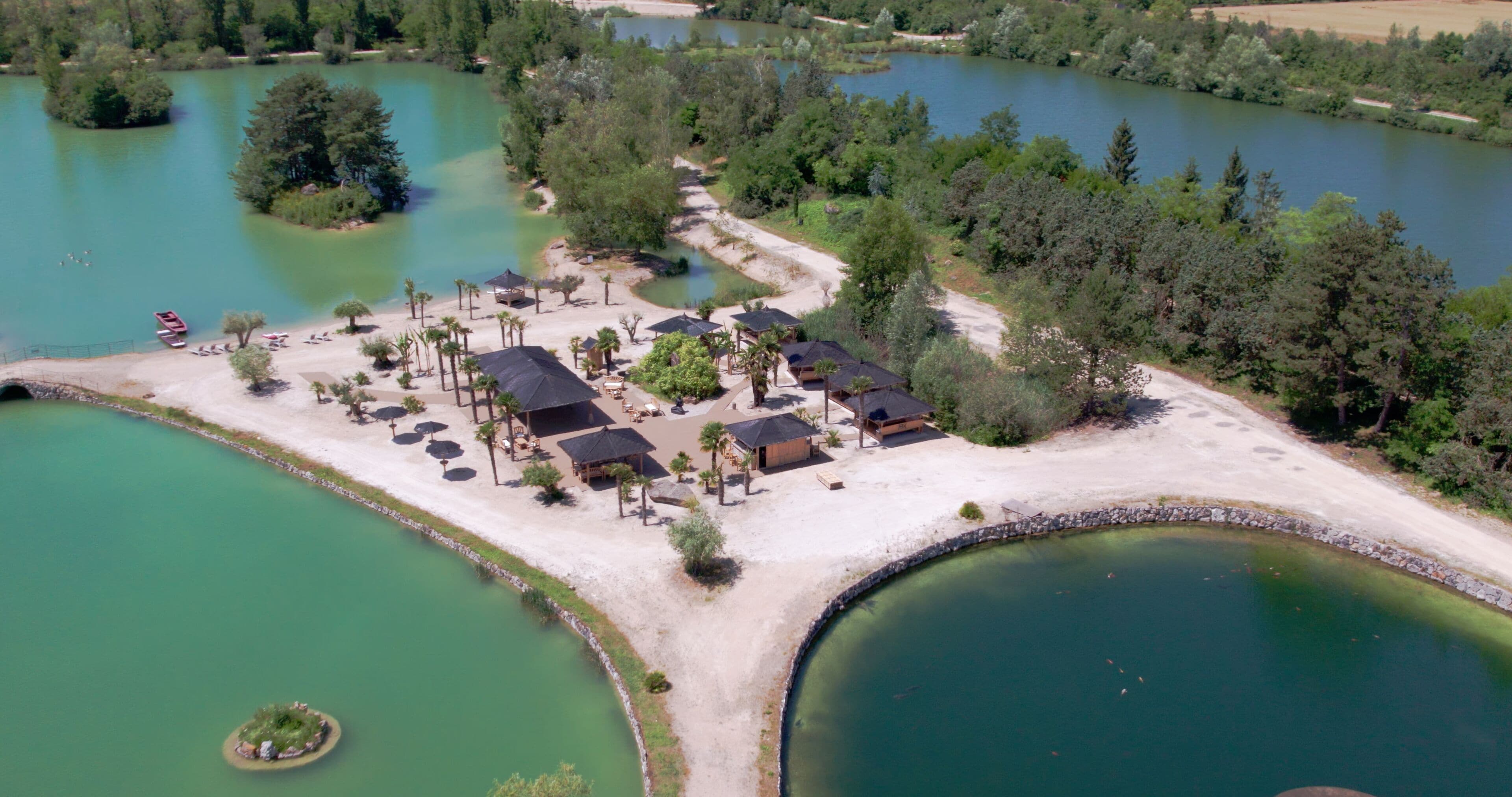 Oversigtsbillede af et feriested ved søen med flere hytter, et centralt pavillon og en velholdt sandstrand.
