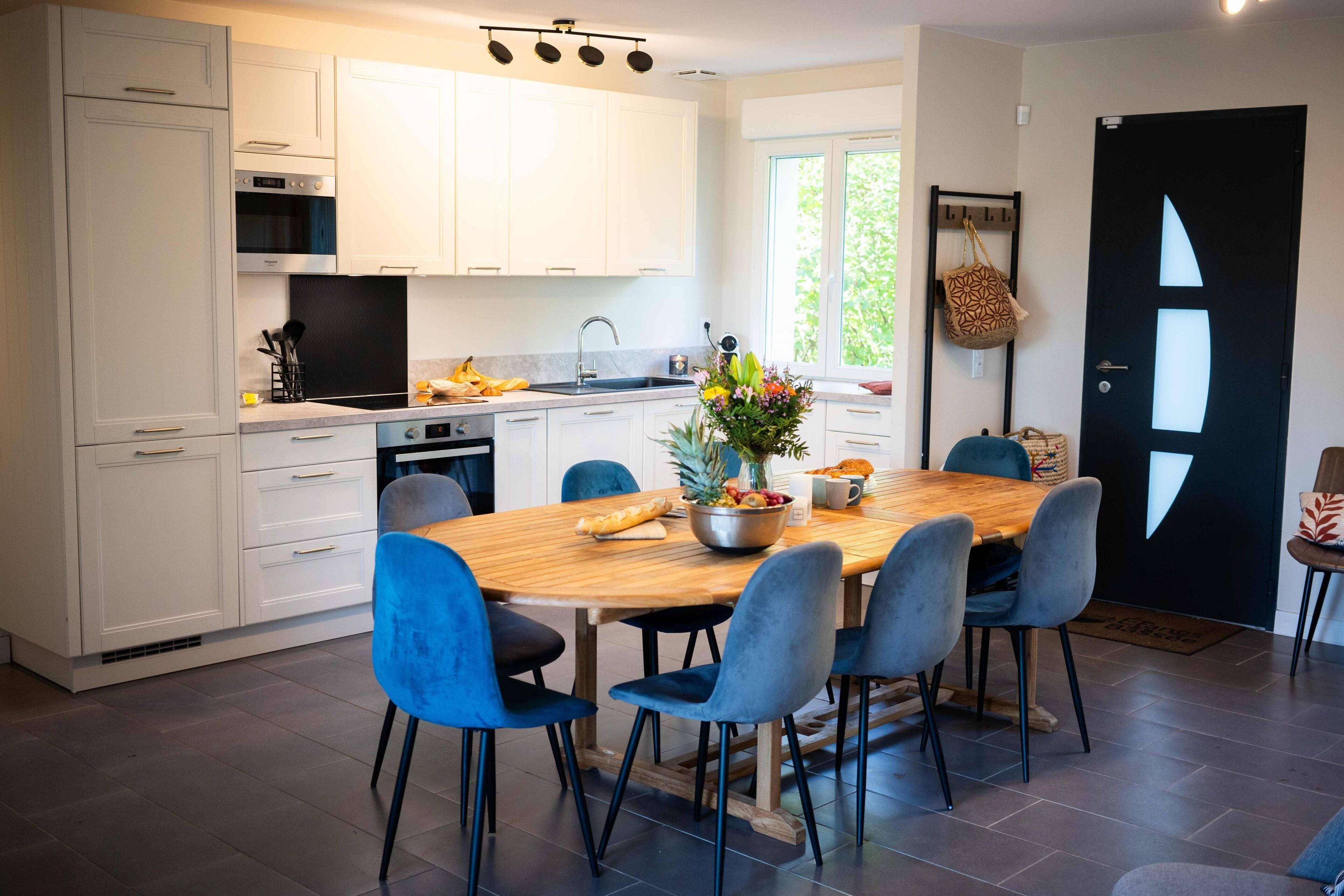 A modern kitchen with white cabinets, a wooden dining table, and blue chairs.