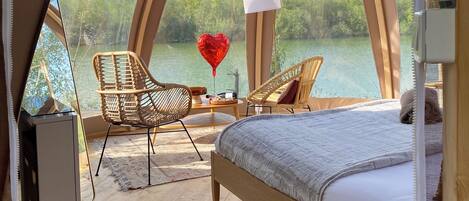 A cozy, circular room with a bed, two wicker chairs, a small table, and a view of a lake.