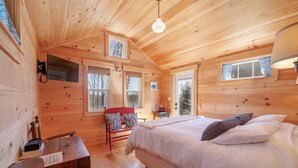 Interior de una cabaña de madera con una cama, un escritorio y una silla.