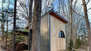Una cabaña de madera con un pequeño porche, rodeada de árboles.