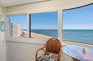 Enjoy a serene view of the beach and city from the comfort of this room, featuring a wicker chair and a small table.