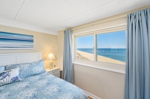 Enjoy a serene beach view from the comfort of this stylish room, featuring a plush bed and a beautiful wall art.
