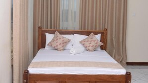 Cama bem arrumada com cabeceira de madeira, duas almofadas estampadas e um cobertor branco.