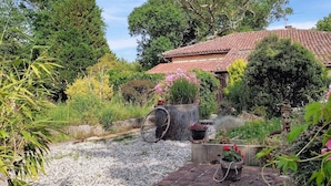 Ein rustikales Haus mit Ziegeldach, umgeben von üppiger Vegetation und blühenden Pflanzen.