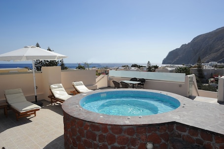 A rooftop terrace with a hot tub, lounge chairs, and a table.