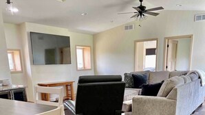 A spacious living area with a large flat-screen TV, a black leather chair, a grey sofa, and a dining table with chairs. - Private Ridge top Cabin/House (Avoca)