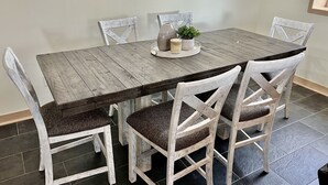 A rustic wooden dining table with a white finish, surrounded by white chairs with dark cushions. - Private Ridge top Cabin/House (Avoca)