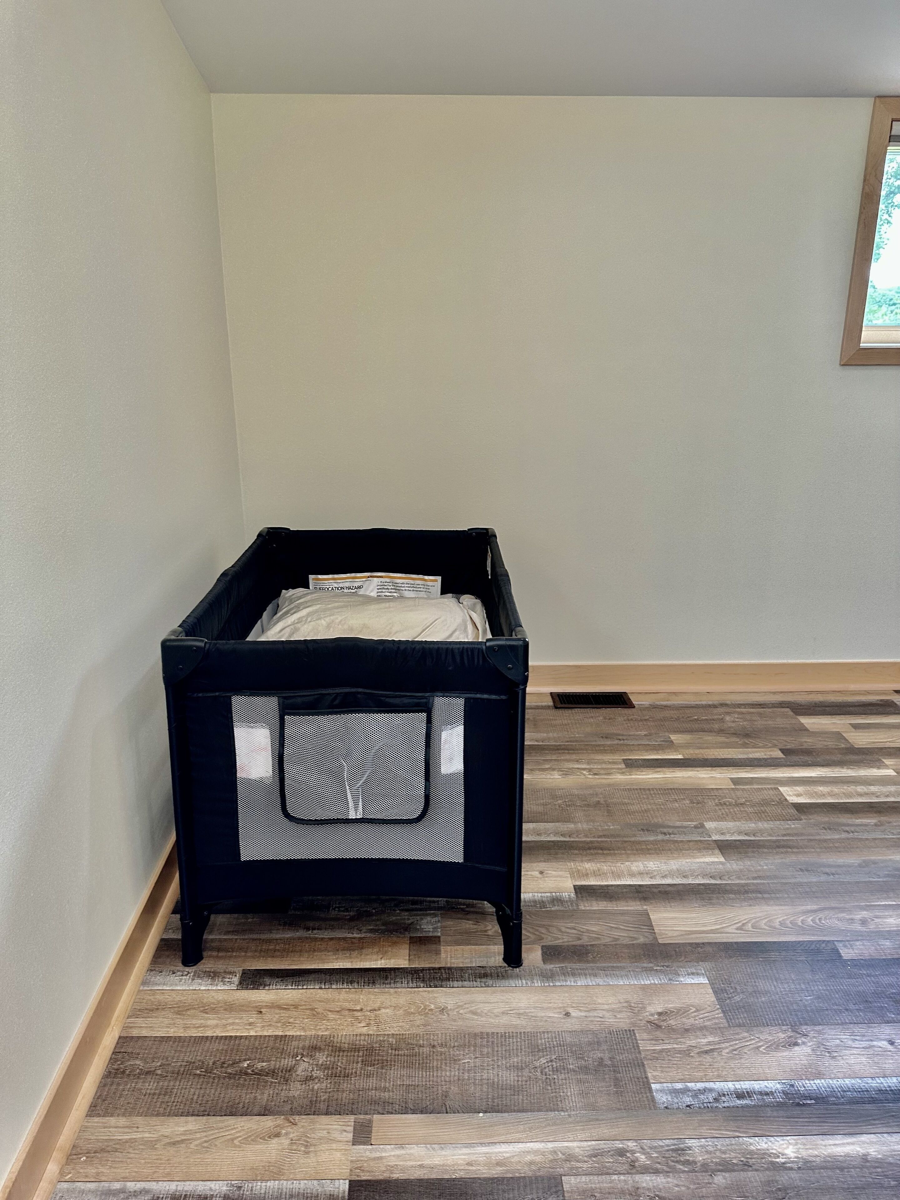 A room with a black storage box against a wall, a herringbone-patterned wooden floor, and a framed picture on the wall.