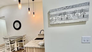 A modern kitchen with a wooden island, pendant lights, a clock, and a motivational sign on the wall. - Private Ridge top Cabin/House (Avoca)