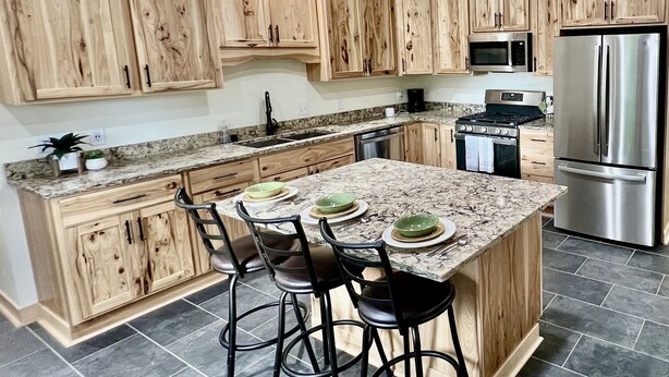 A kitchen with wooden cabinets, a granite countertop, a stainless steel refrigerator, and bar stools. - Private Ridge top Cabin/House (Avoca)