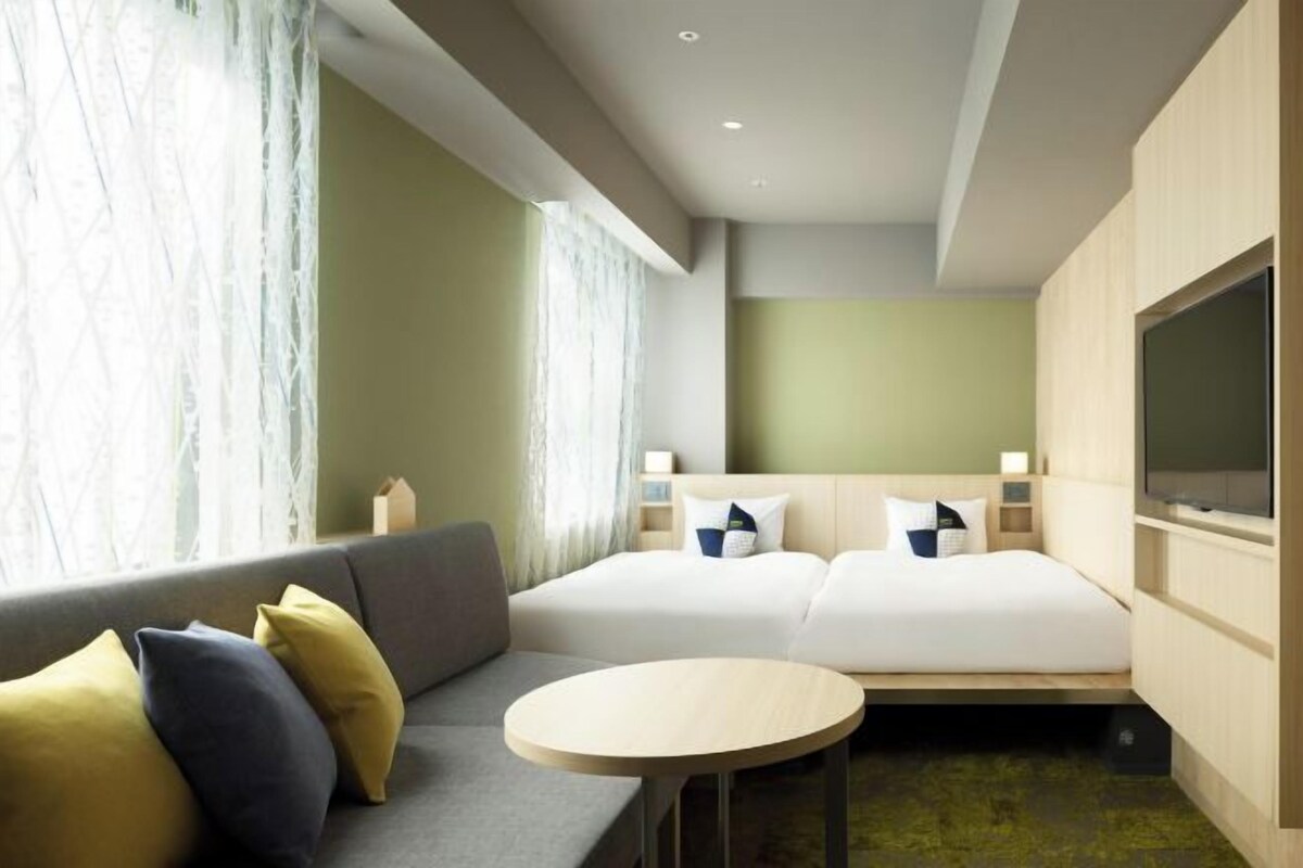 A hotel room with a sofa, two beds, a TV, and a small table.