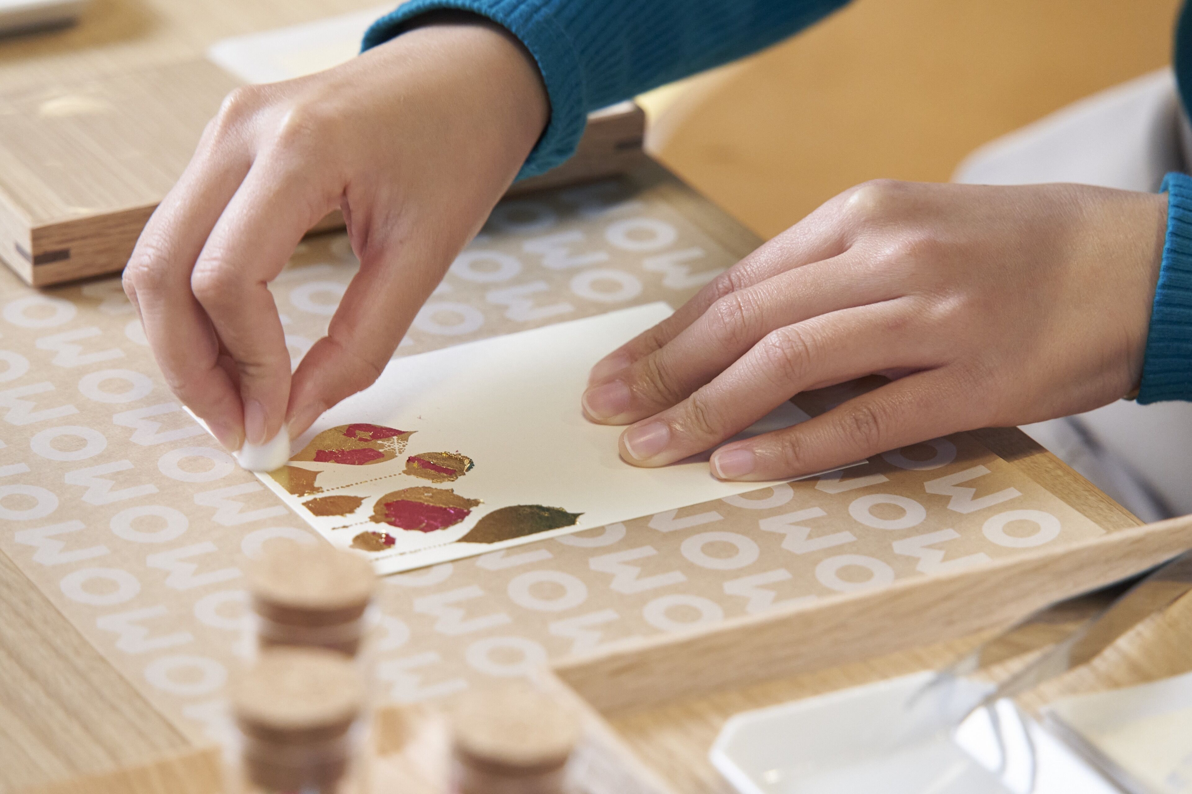 Hands using a wooden tool on a paper with a pattern.