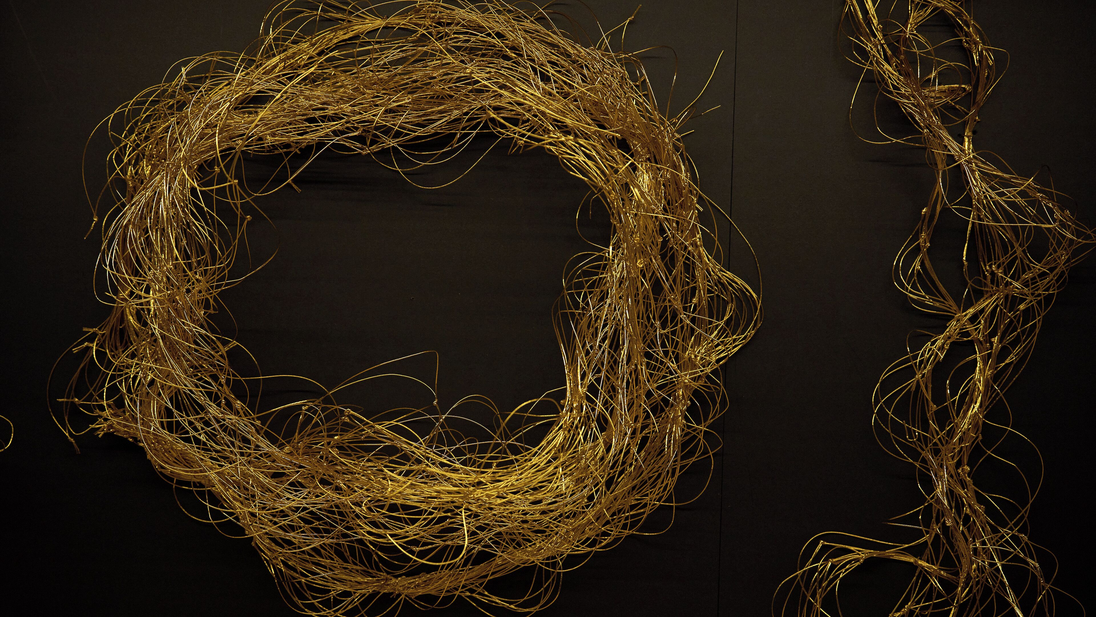 A tangled golden wire sculpture against a dark background.
